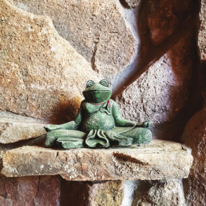 A frog statue sitting cross-legged on rocks, in meditation mode.
