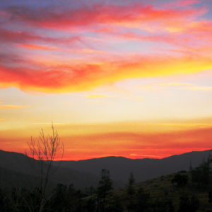 An orange sky above hills and trees.