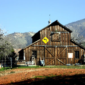 A painterly image of a barn in the mountains, with a left turn sign.