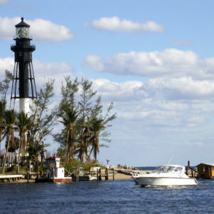 A lighthouse surrounded by trees, clouds in the sky, and a boat in the water